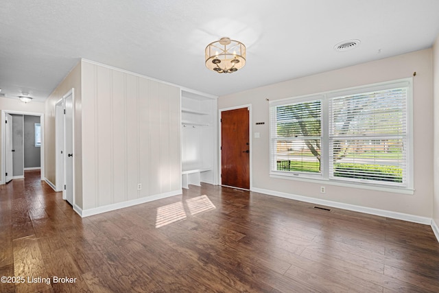 empty room featuring visible vents, a notable chandelier, wood finished floors, and baseboards