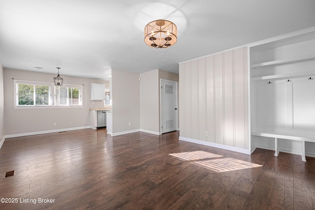 unfurnished living room featuring a chandelier, visible vents, dark wood-style flooring, and baseboards