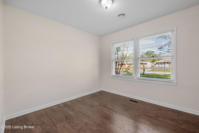 unfurnished room with visible vents, dark wood finished floors, and baseboards