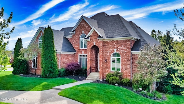 traditional-style home featuring a shingled roof, a front lawn, and brick siding