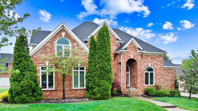 view of front facade with brick siding, a shingled roof, and a front yard