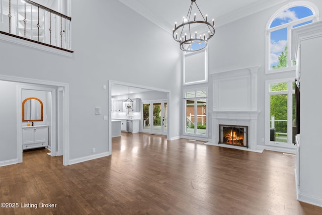 unfurnished living room with an inviting chandelier, baseboards, a fireplace with flush hearth, wood finished floors, and a towering ceiling