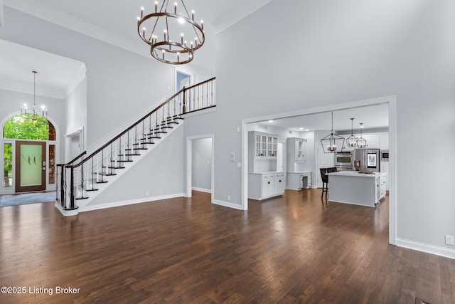 unfurnished living room with dark wood-type flooring, a towering ceiling, a notable chandelier, and stairway