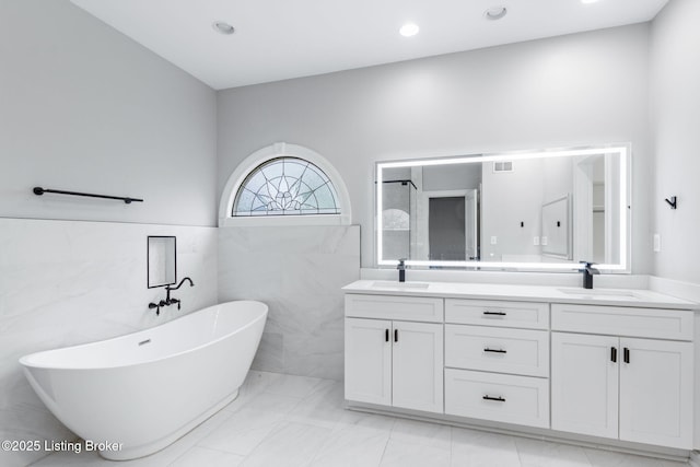 bathroom with double vanity, a sink, a freestanding tub, and visible vents