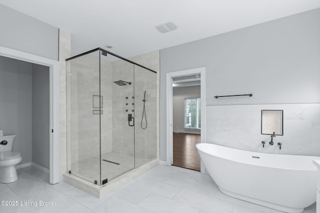 full bath with a freestanding bath, toilet, marble finish floor, baseboards, and a stall shower
