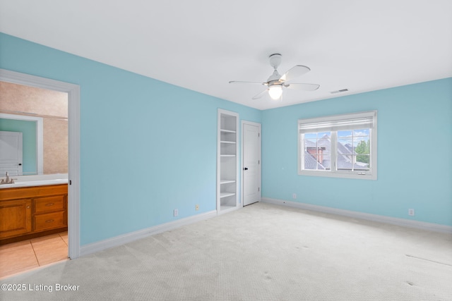 unfurnished bedroom featuring a sink, baseboards, light carpet, and visible vents