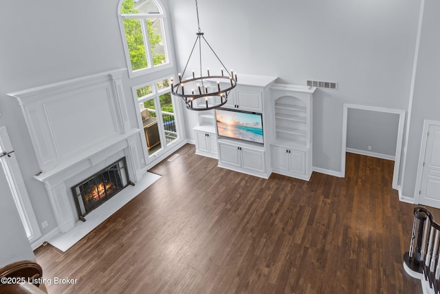 unfurnished living room featuring an inviting chandelier, visible vents, a high ceiling, dark wood-style floors, and a premium fireplace