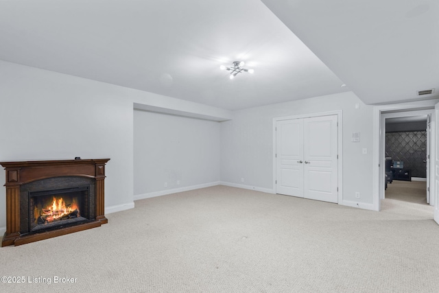 unfurnished living room with a warm lit fireplace, light colored carpet, baseboards, and visible vents