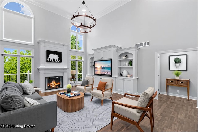 living area with visible vents, dark wood-style flooring, a towering ceiling, and a lit fireplace