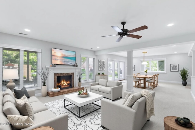 living room featuring a warm lit fireplace, light colored carpet, a healthy amount of sunlight, and visible vents