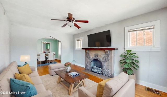 living area featuring arched walkways, ceiling fan with notable chandelier, wood finished floors, and visible vents