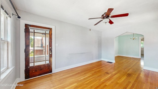 empty room featuring a healthy amount of sunlight, arched walkways, light wood finished floors, and visible vents