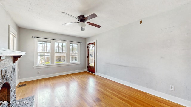unfurnished living room with wood-type flooring, a ceiling fan, baseboards, and a fireplace