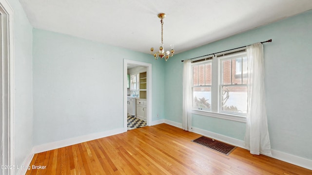 unfurnished room with baseboards, a notable chandelier, wood finished floors, and visible vents