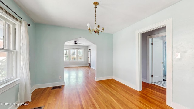 unfurnished dining area featuring visible vents, baseboards, arched walkways, light wood finished floors, and ceiling fan with notable chandelier
