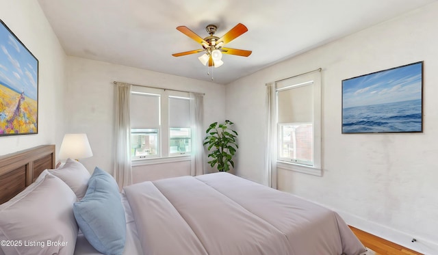 bedroom featuring a ceiling fan, baseboards, multiple windows, and wood finished floors