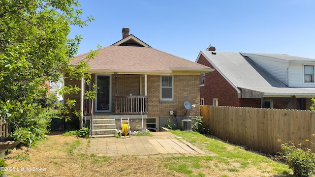 back of house featuring fence, brick siding, a chimney, central air condition unit, and covered porch