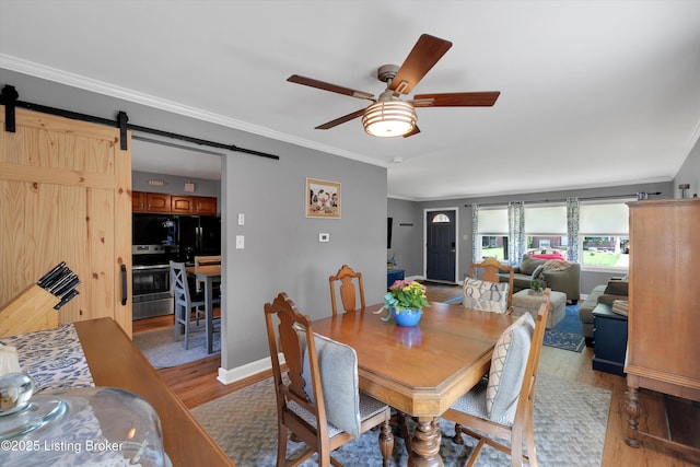 dining space featuring ceiling fan, a barn door, light wood-type flooring, and ornamental molding