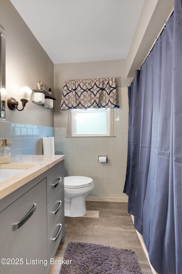 bathroom featuring tile walls, vanity, toilet, a wainscoted wall, and wood finished floors