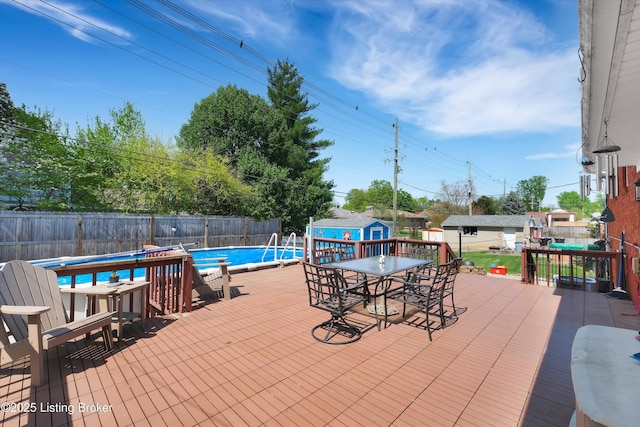view of swimming pool with a fenced in pool, a fenced backyard, outdoor dining space, a deck, and a storage unit