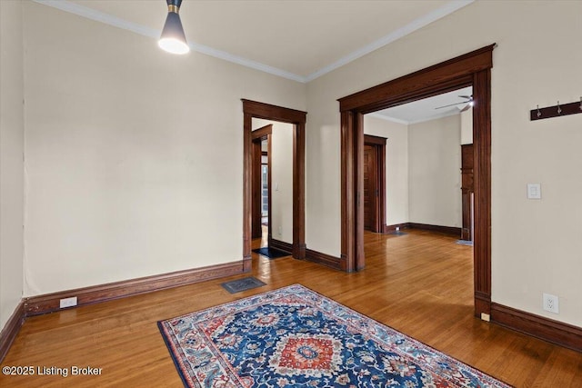 spare room featuring baseboards, visible vents, wood finished floors, and crown molding