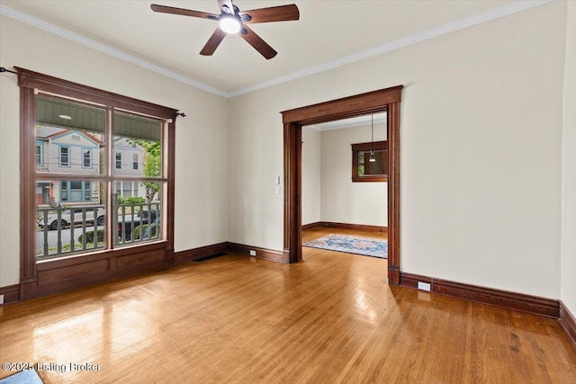 empty room featuring light wood-style flooring, ceiling fan, visible vents, baseboards, and ornamental molding