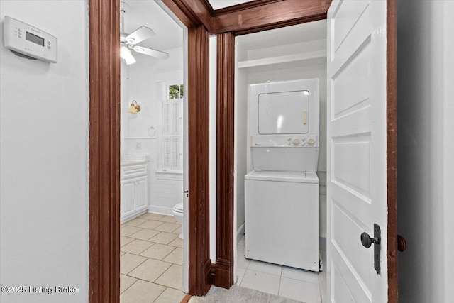 clothes washing area featuring light tile patterned floors, ceiling fan, stacked washer / dryer, and laundry area