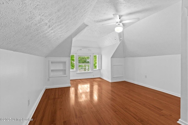 additional living space featuring built in shelves, lofted ceiling, baseboards, a textured ceiling, and wood finished floors