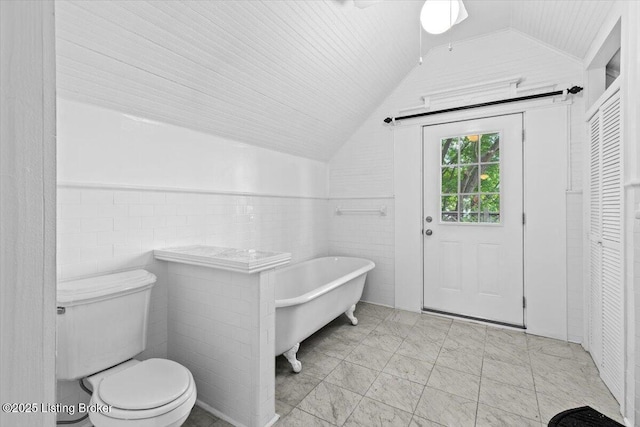 bathroom with wainscoting, vaulted ceiling, tile walls, toilet, and a soaking tub