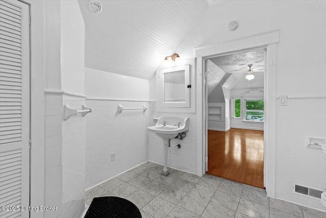 bathroom featuring tile walls, a wainscoted wall, a ceiling fan, visible vents, and lofted ceiling