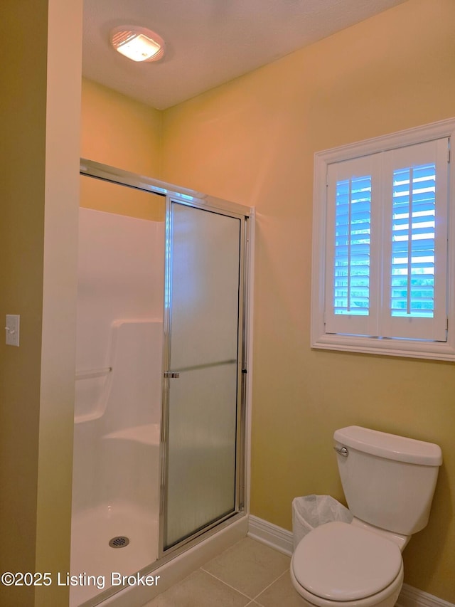 bathroom with toilet, a shower stall, tile patterned floors, and baseboards