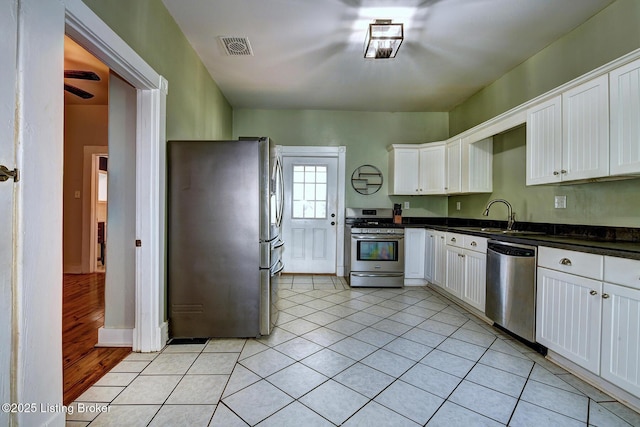 kitchen featuring stainless steel appliances, dark countertops, a sink, white cabinetry, and light tile patterned flooring