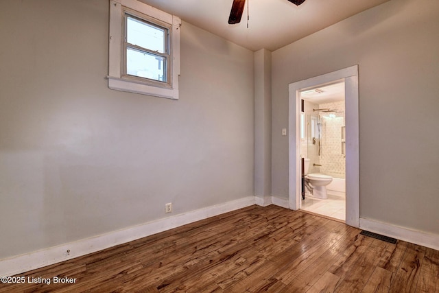 empty room featuring ceiling fan, hardwood / wood-style floors, visible vents, and baseboards