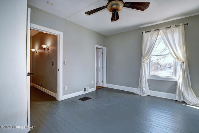 empty room featuring dark wood-style floors, visible vents, a ceiling fan, and baseboards