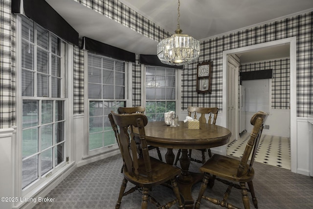 carpeted dining space featuring an inviting chandelier and wallpapered walls