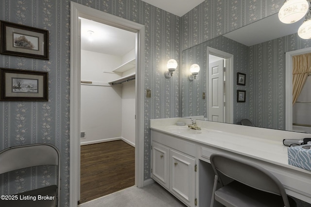 bathroom featuring a walk in closet, visible vents, wood finished floors, vanity, and baseboards