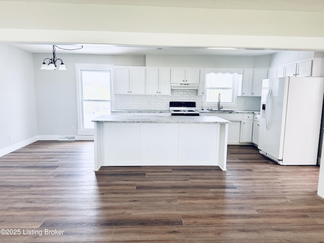 kitchen with white cabinets, a chandelier, under cabinet range hood, white appliances, and backsplash