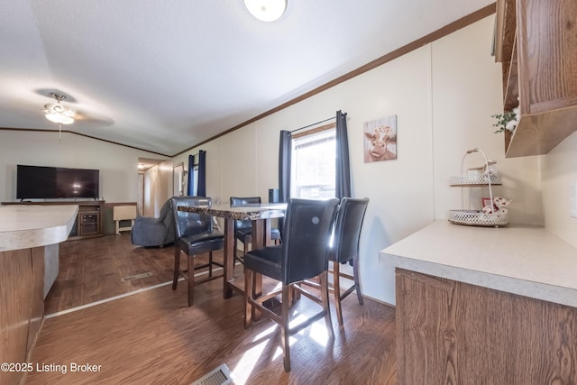 dining room featuring crown molding, a ceiling fan, dark wood-type flooring, and vaulted ceiling