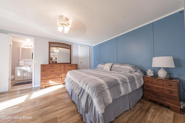 bedroom with connected bathroom, light wood-style flooring, a textured ceiling, and a decorative wall