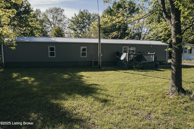 back of property with a wooden deck, a yard, and metal roof
