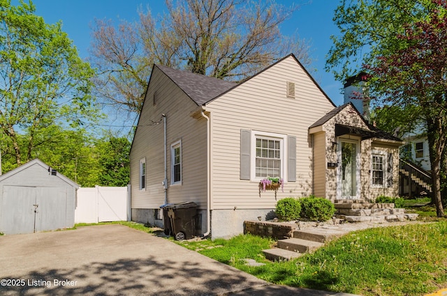 bungalow-style home with fence, a storage unit, a gate, an outbuilding, and a chimney