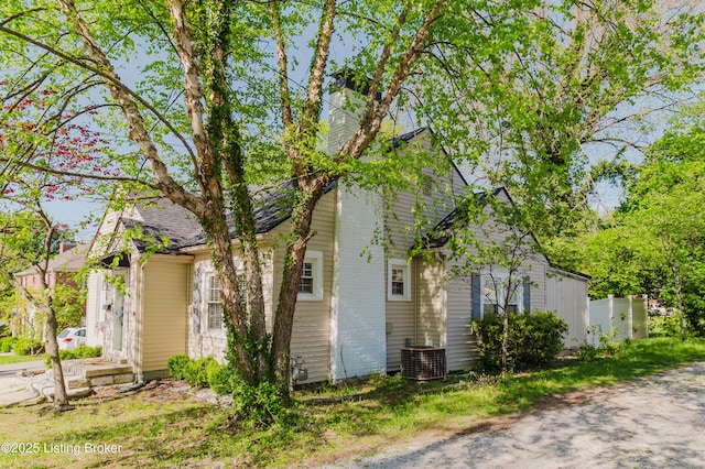 view of side of home featuring central AC unit, fence, and a chimney