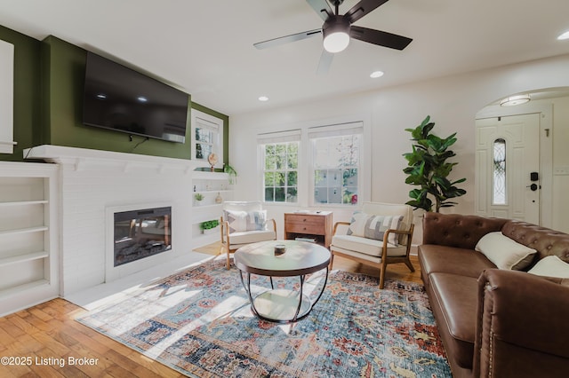 living area with ceiling fan, arched walkways, a brick fireplace, wood finished floors, and recessed lighting
