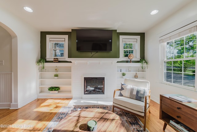 living area featuring arched walkways, a brick fireplace, wood finished floors, baseboards, and recessed lighting