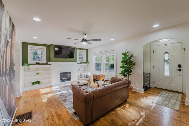 living area featuring a glass covered fireplace, arched walkways, a ceiling fan, and hardwood / wood-style flooring