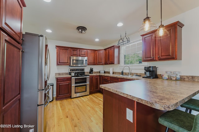 kitchen with dark brown cabinets, a sink, light wood finished floors, a peninsula, and stainless steel appliances