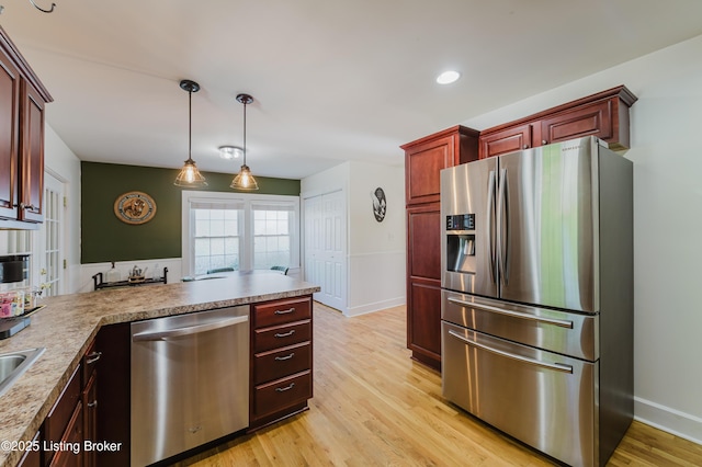 kitchen with hanging light fixtures, dark brown cabinets, light wood finished floors, a peninsula, and stainless steel appliances