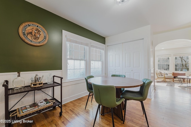 dining area with wood finished floors, arched walkways, and a wainscoted wall