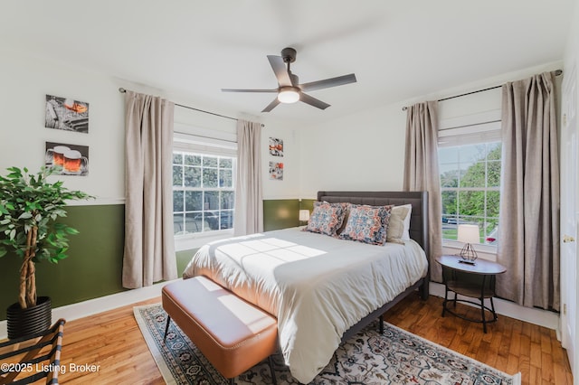 bedroom with ceiling fan, wood finished floors, and multiple windows