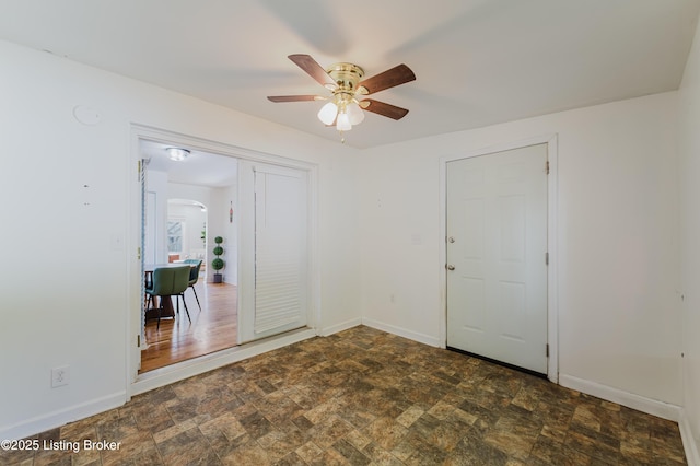 empty room featuring baseboards, arched walkways, stone finish flooring, and ceiling fan